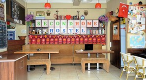 A hostel with a central seating area, tables, and chairs. There are shelves with books and decorative items. A sign above the seating area reads "SECOND HOME HOSTEL". - Second Home Hostel (Istanbul)