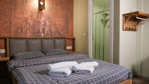 Une chambre à coucher comprenant un lit, une tête de lit en bois, une table de chevet, un porte-serviettes et un espace douche.