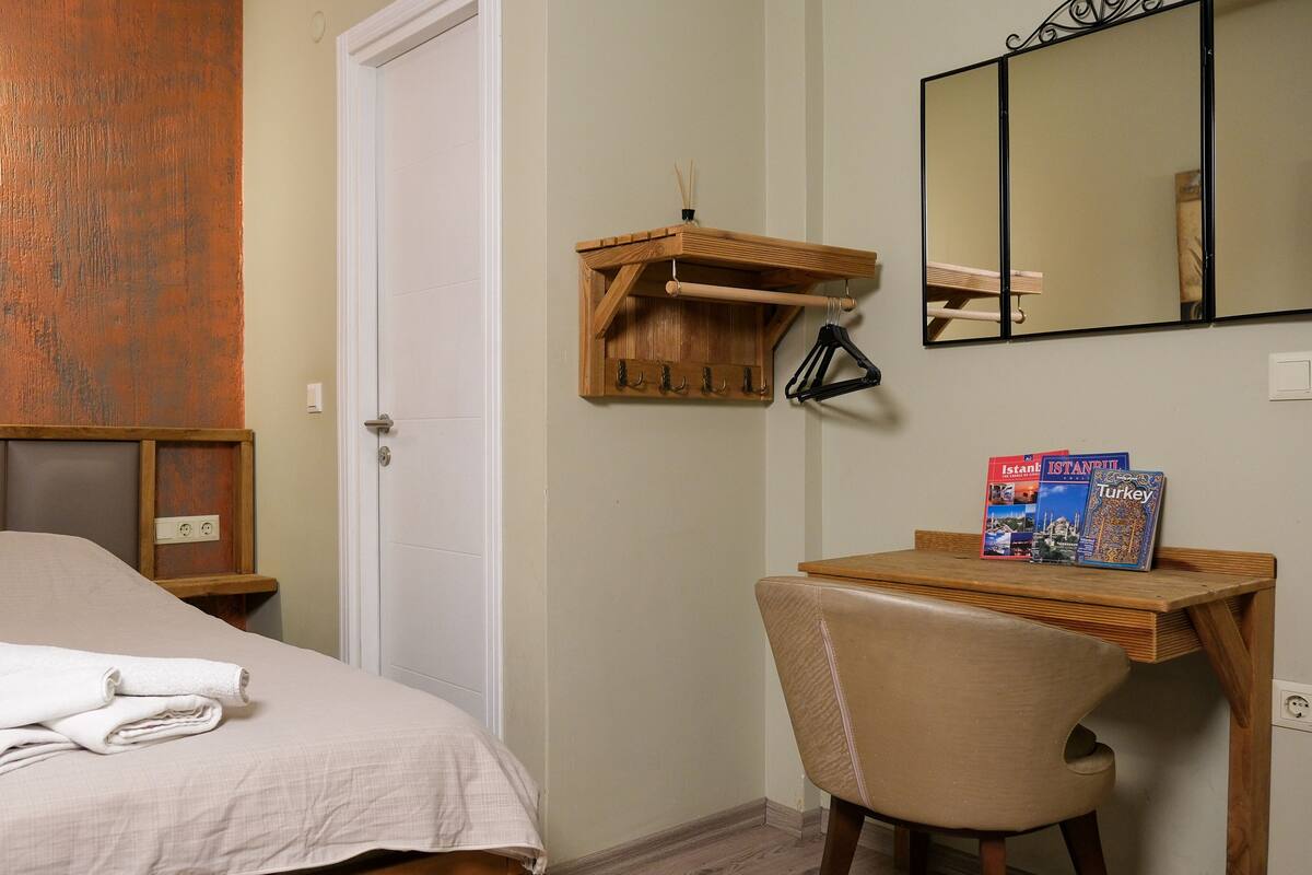 A bedroom with a bed, a bedside table, a chair, a small wooden shelf, and a mirror.