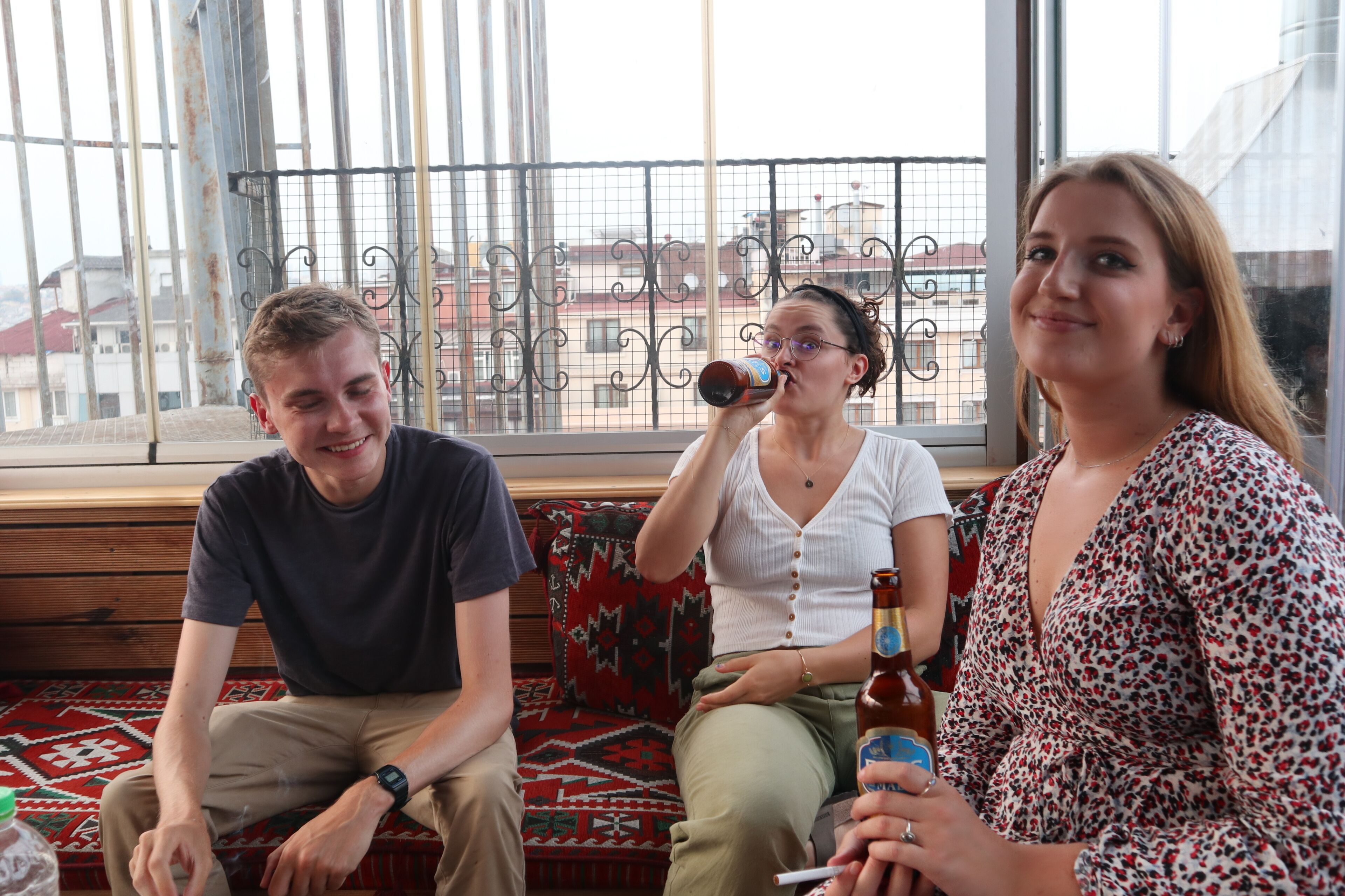 Three people sitting on a bench with a view of buildings through a window.