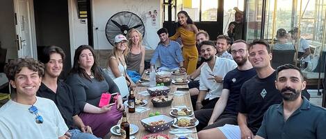 A group of people seated around a table with various dishes, in an outdoor setting with a covered patio.