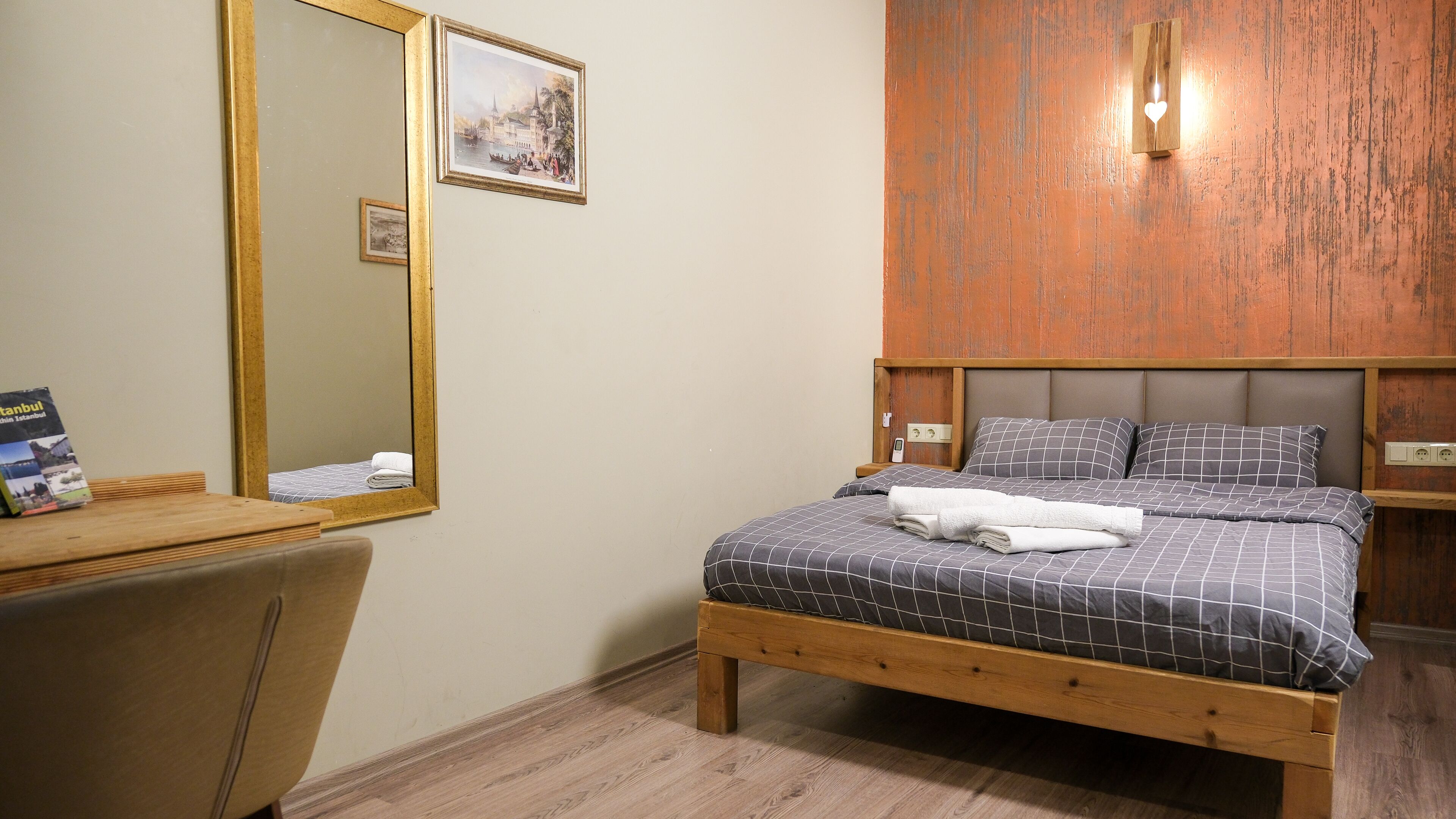 A bedroom with a wooden bed, a nightstand, a mirror, and a wall-mounted light fixture.