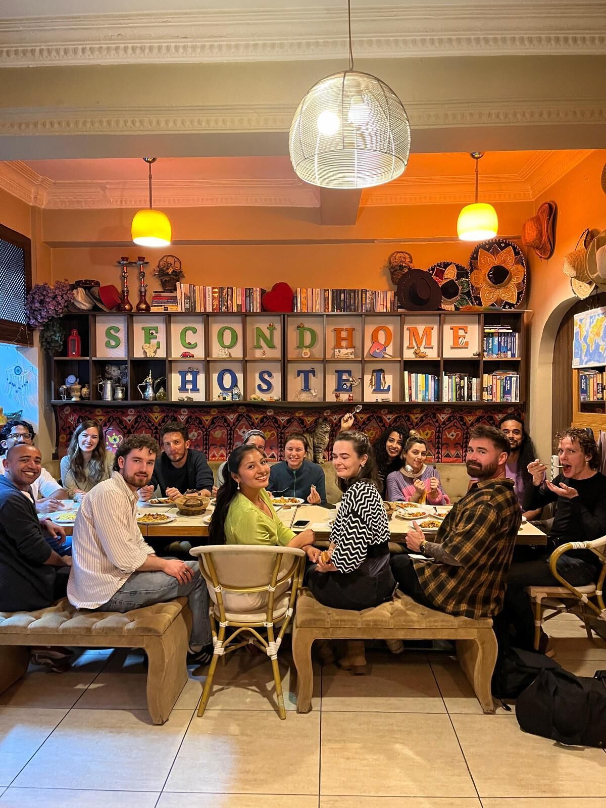 A group of people dining in a restaurant with a bookshelf displaying the word 'SECOND HOME'.