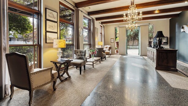Un vestíbulo amplio con piso de concreto pulido, ventanas grandes con marcos de madera, un candelabro y una zona de estar con mesa y sillas.