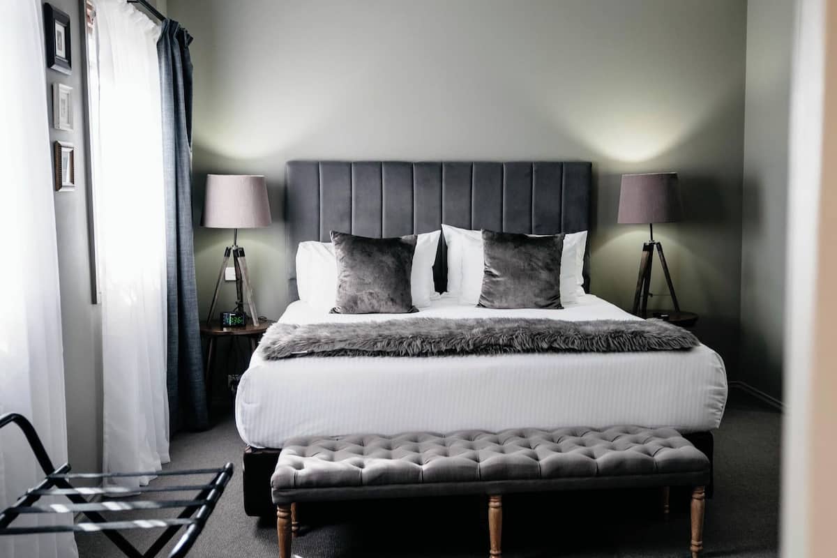 A neatly arranged bedroom with a large bed, two bedside lamps, a small bedside table, and a bench at the foot of the bed.