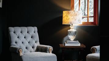 Una habitación con un sillón tapizado, una mesita con lámpara y una ventana con vistas a árboles.