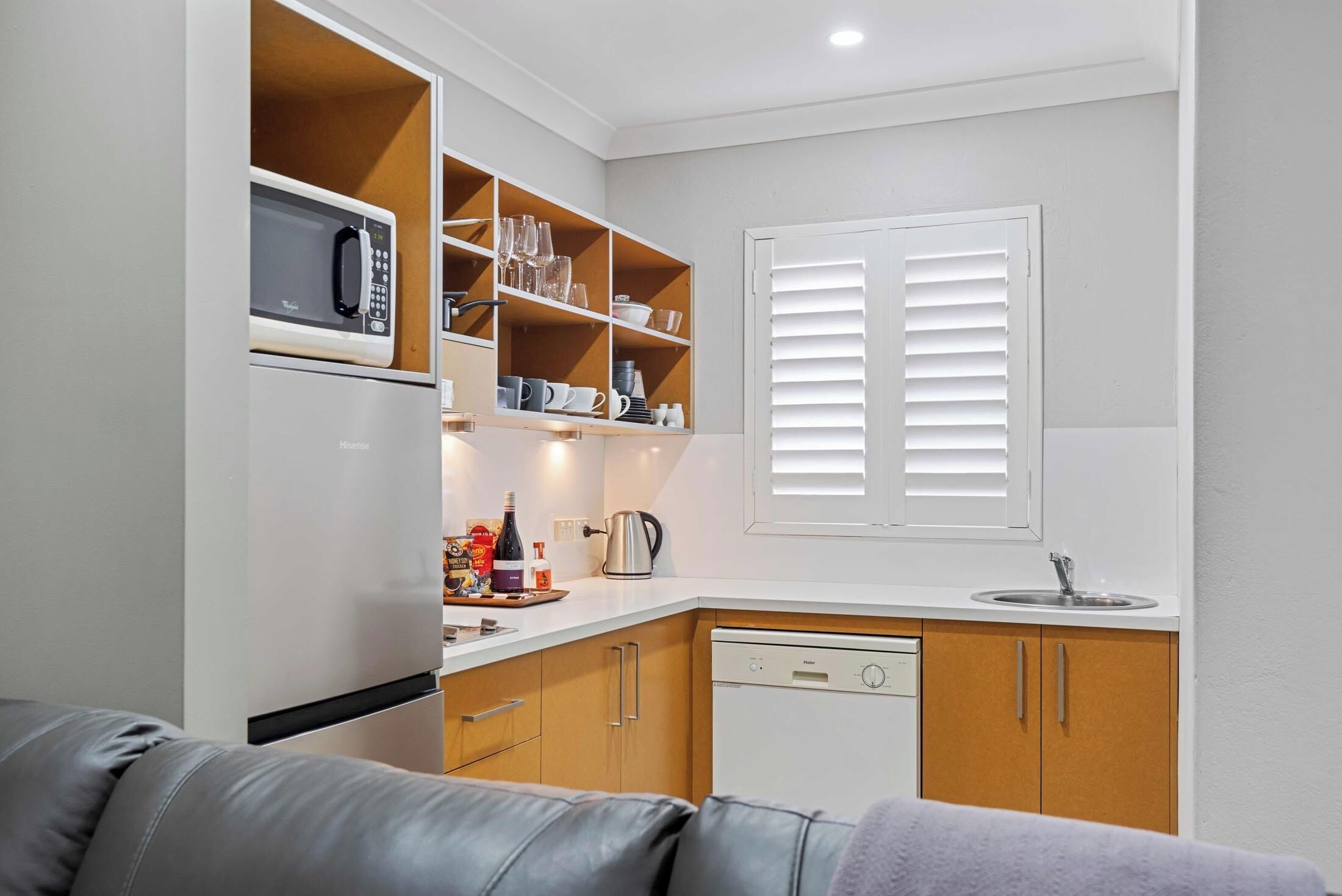 A compact kitchen with a microwave, shelves with glassware, a sink, and a dishwasher.