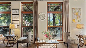 Una habitación con ventanas amplias, techo de madera, un reloj, un jarrón con flores y una silla.