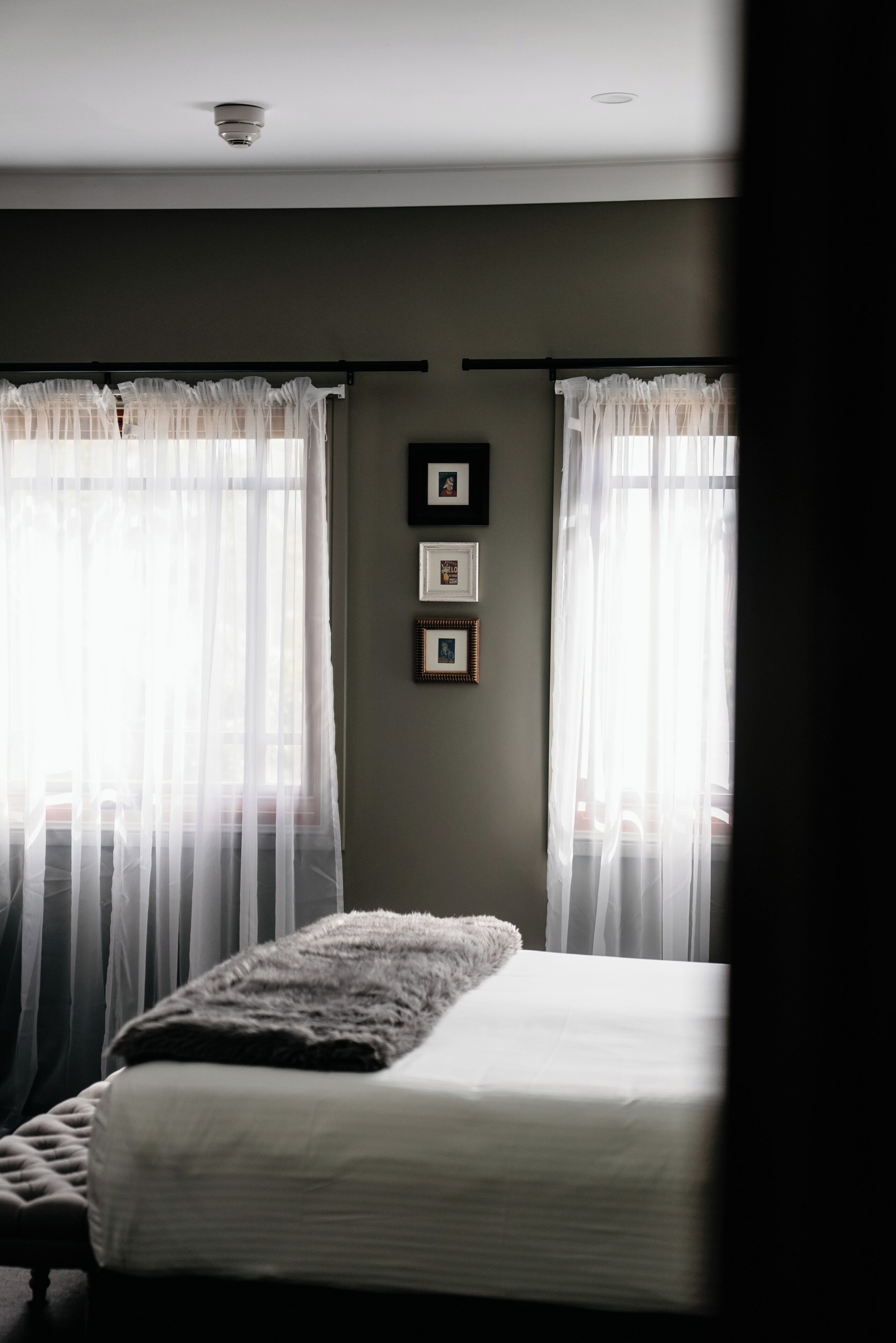 Een slaapkamer met een bed, dunne gordijnen en lijstwerken aan de muur.
