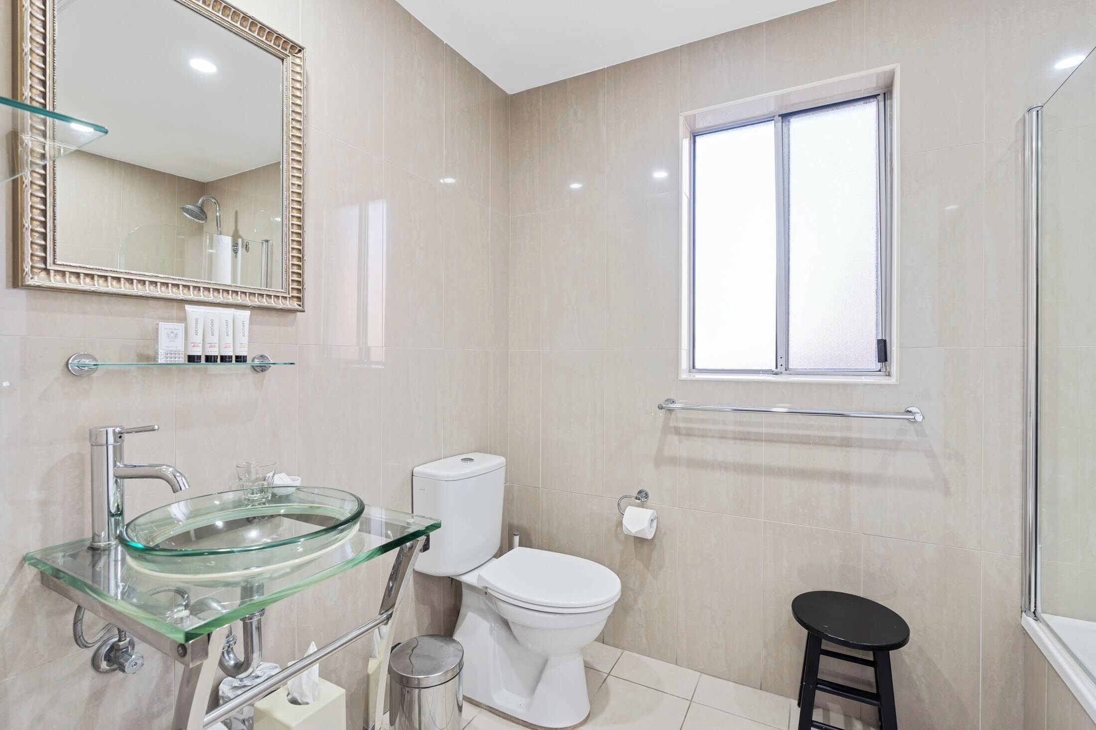 A modern bathroom with a glass sink, white toilet, and a window.