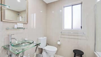 A modern bathroom with a glass sink, white toilet, and a window.