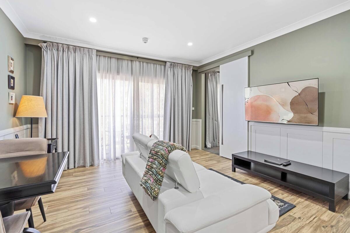 A modern living room with a white sofa, a black coffee table, a lamp, and a TV on a white cabinet.