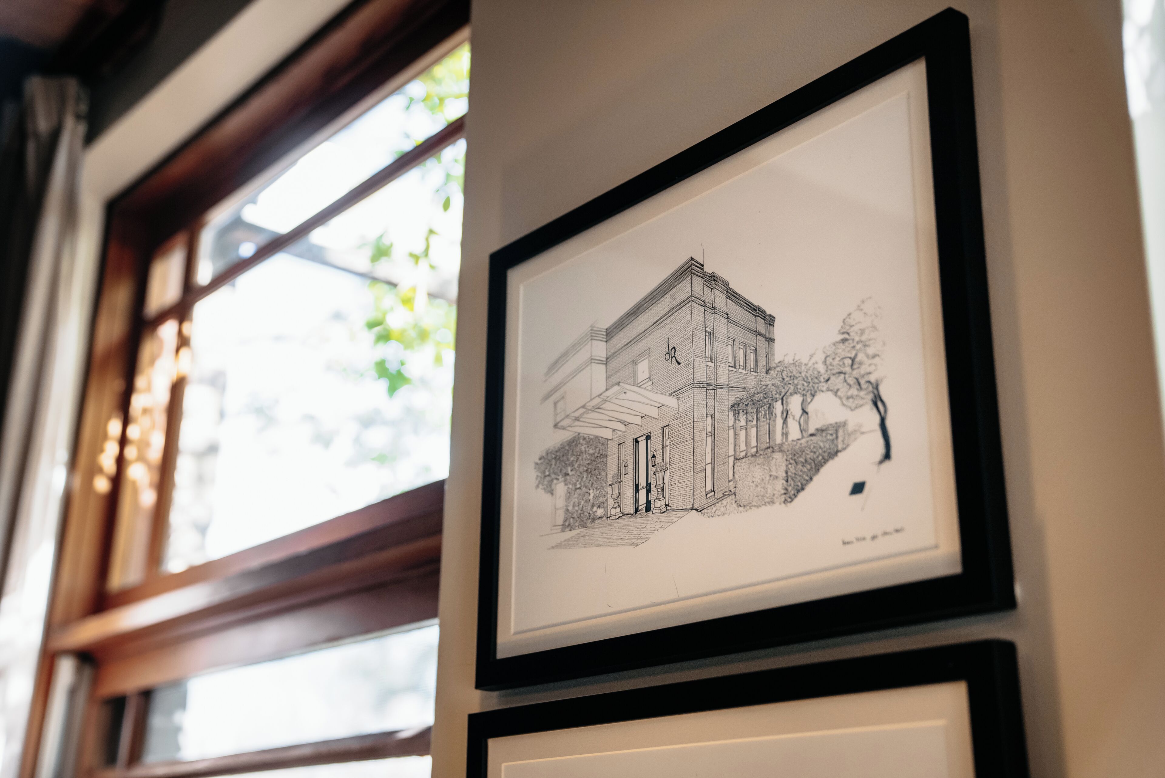 A framed architectural drawing of a building with a balcony and a door, mounted on a wall.