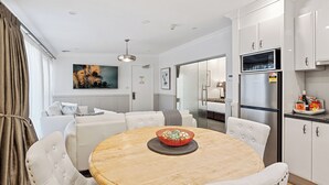 Una cocina moderna con armarios blancos, un refrigerador de acero inoxidable y un comedor con una mesa redonda de madera y sillas tapizadas en blanco.