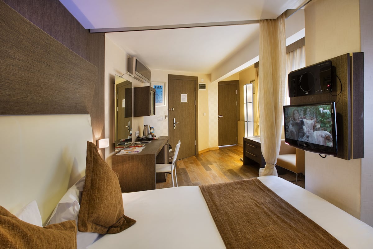 Hotellihuone, jossa on sänky, työpöytä, tuoli, televisio ja kylpyhuone, joka näkyy avoimesta ovesta.