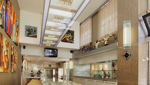 Un moderno vestíbulo de hotel con un mostrador de recepción central, zonas de estar, obras de arte en las paredes y una pantalla de televisión.