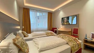Habitación de hotel con dos camas, televisión, escritorio y ventana con cortinas.