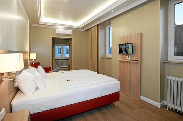 Habitación de hotel con una cama grande, un televisor montado en la pared y una ventana con vistas.