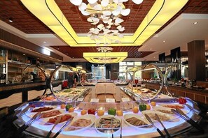 Un bufé con diversas opciones de comida, un espacio central para sentarse y un moderno candelabro.