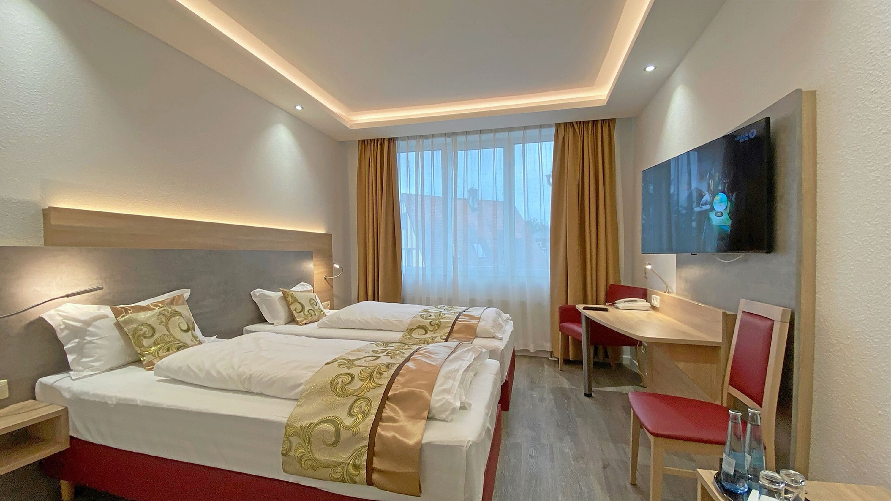 Habitación de hotel con una cama grande, un escritorio, una silla y un televisor instalado en la pared.