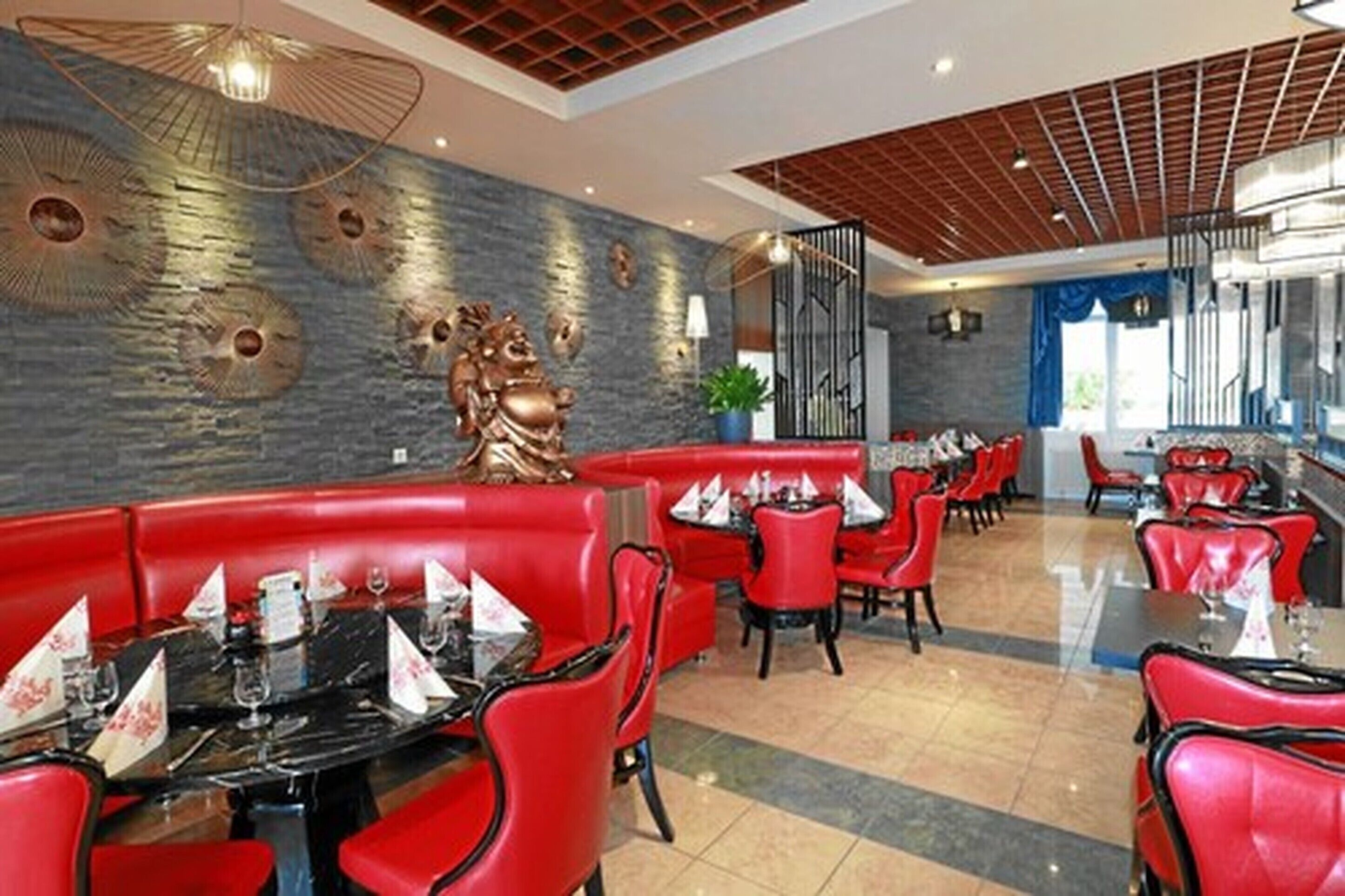 A restaurant with red booths and tables, a stone wall with decorative elements, and a modern ceiling design.