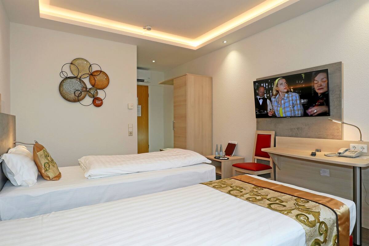 Una habitación de hotel con dos camas, un escritorio con teléfono y una televisión montada en la pared.