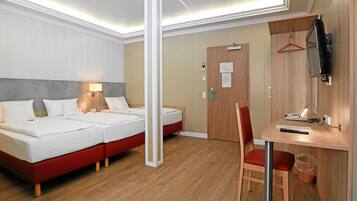 Habitación de hotel con cama doble, escritorio con silla, televisor montado en la pared y puerta de madera.