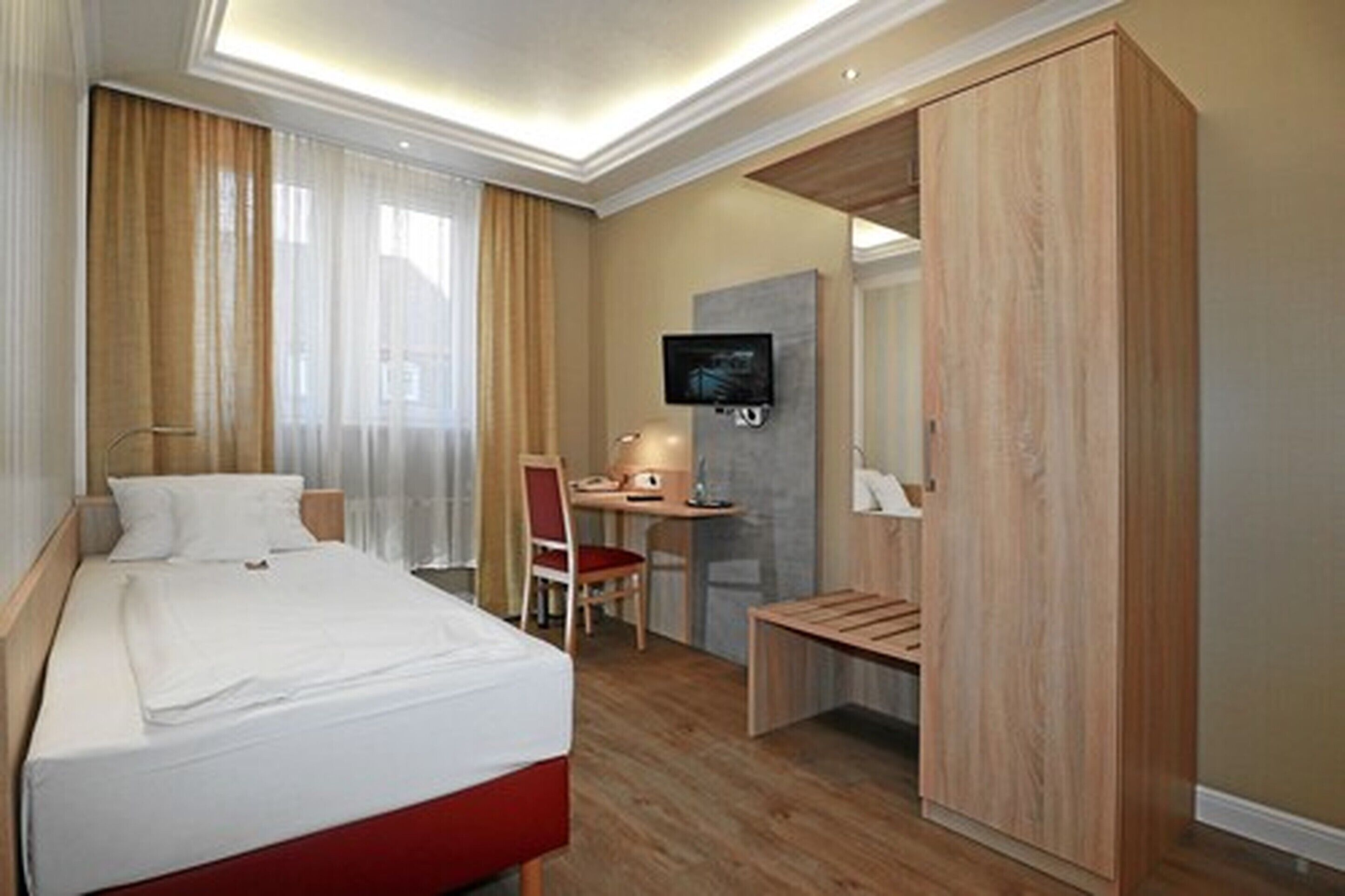 Habitación de hotel con cama, escritorio, silla, televisor y armario.