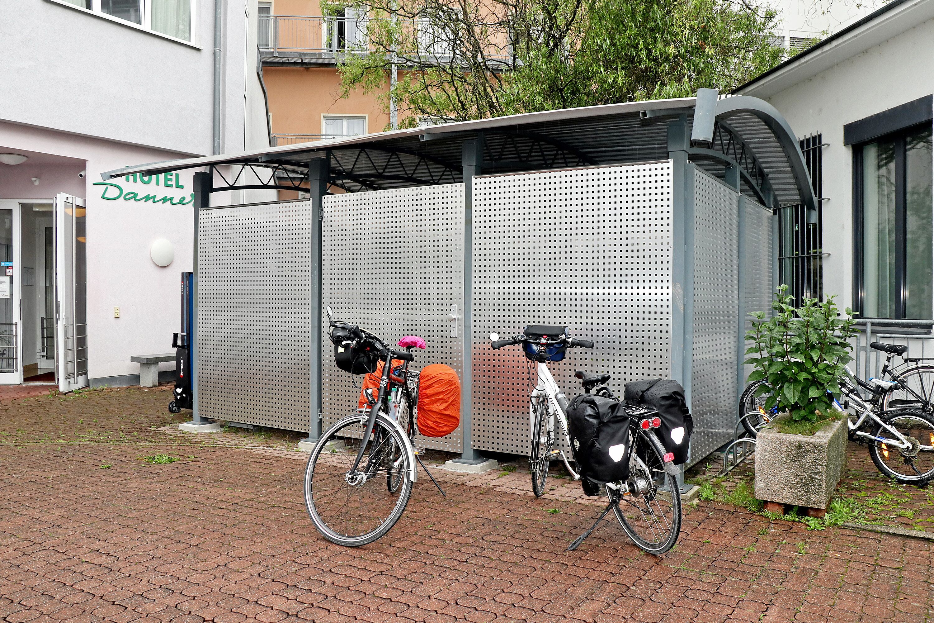 A covered waiting area with bicycles parked outside a hotel named "Hotel Dannis."