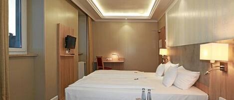 A hotel room with a large bed, bedside tables, a desk, and a TV.