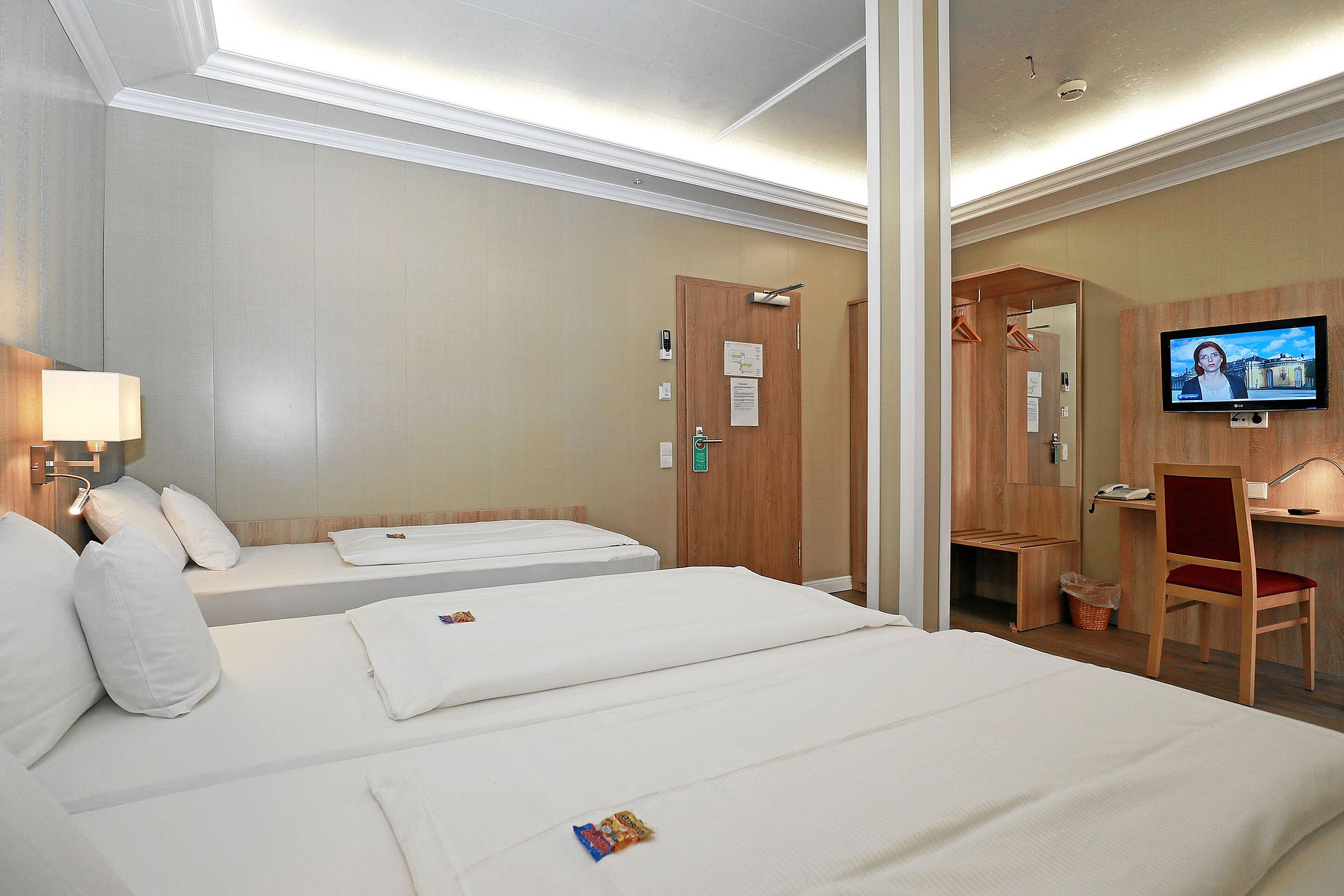 Habitación de hotel con dos camas, un escritorio, una silla, un televisor y un espejo.