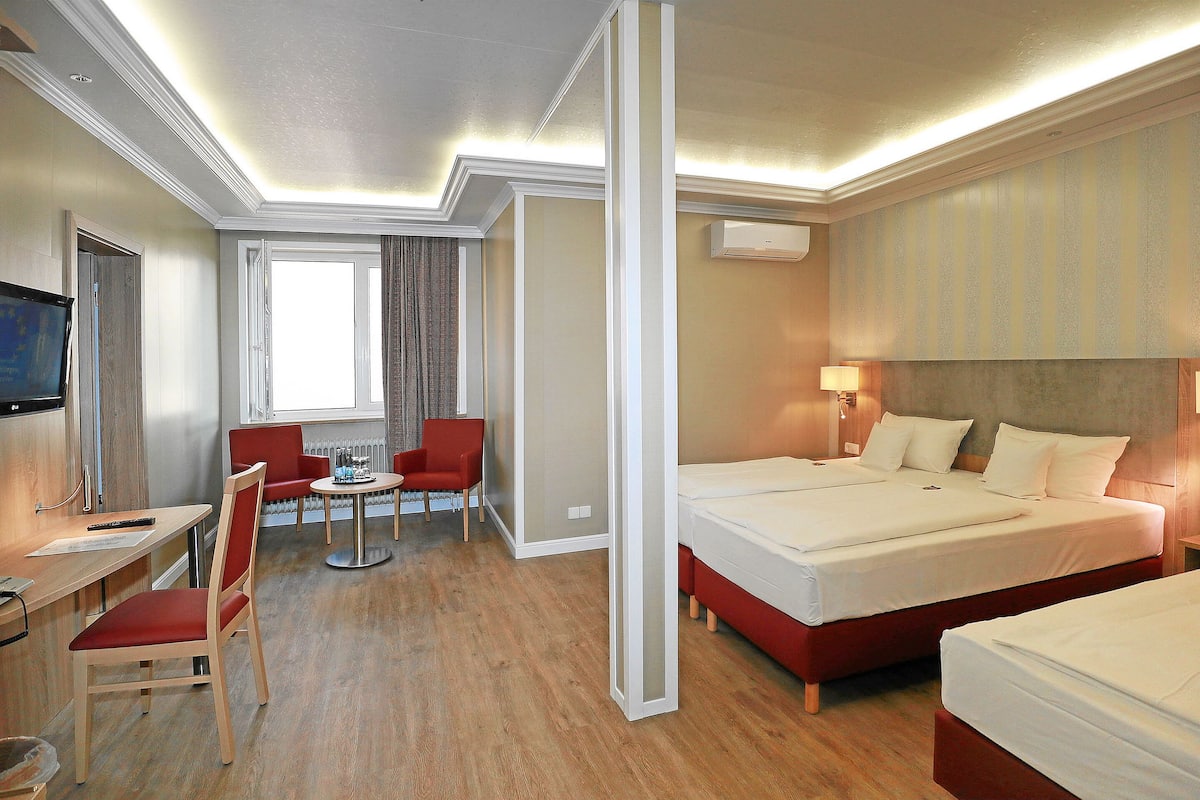 Habitación de hotel con dos camas, un escritorio con silla, una mesita y un televisor.