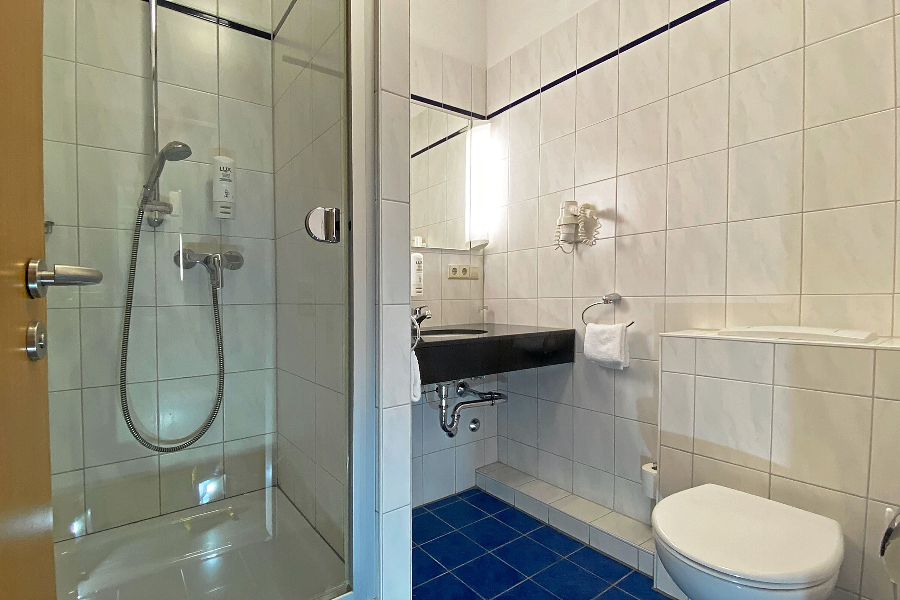 Et moderne badeværelse med bruseniche i glas, et sort vaskeskab og et hvidt toilet.