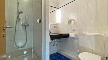 Et moderne badeværelse med bruseniche i glas, et sort vaskeskab og et hvidt toilet.
