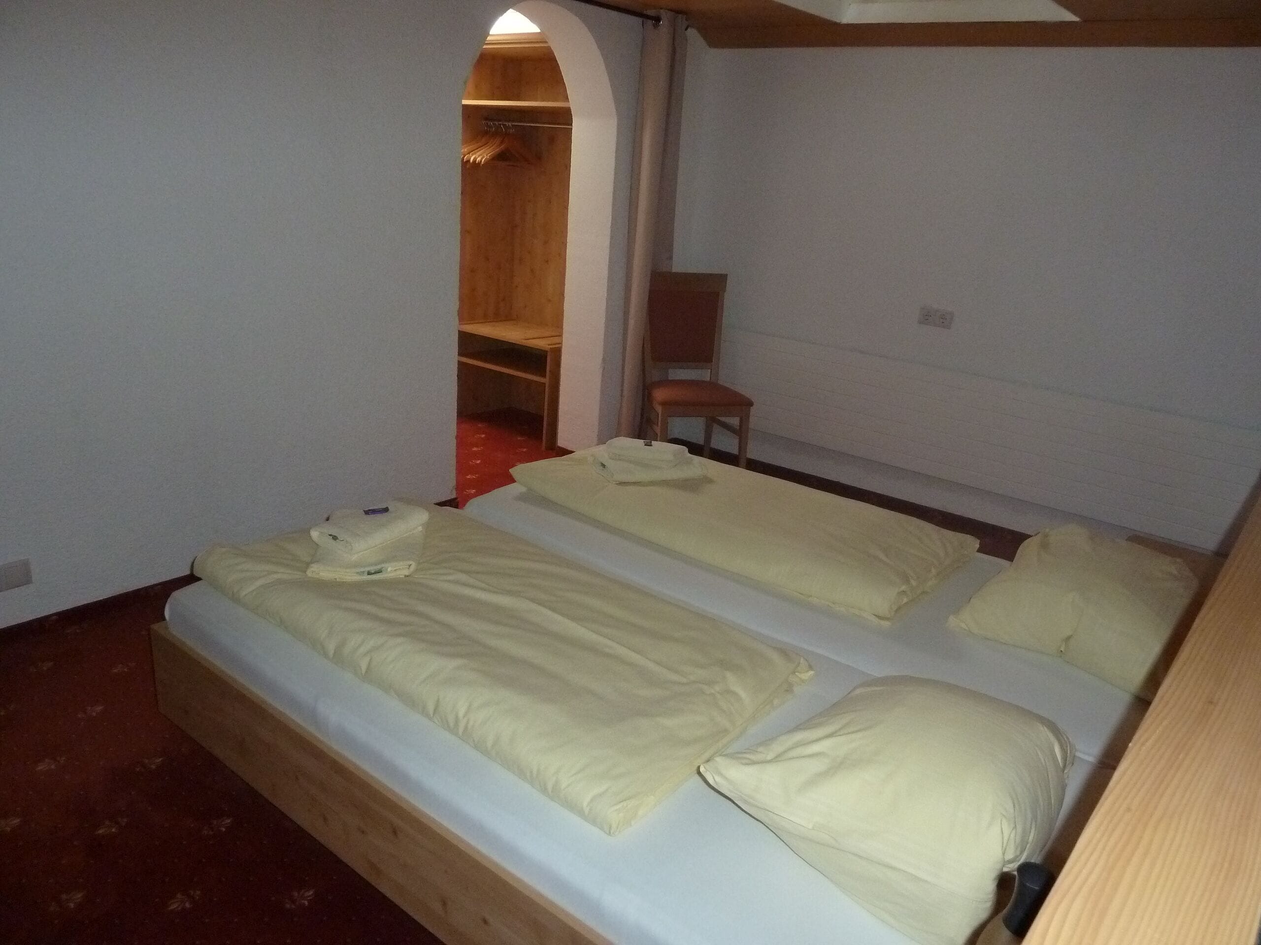 Une petite chambre d’hôtel composée d’une seule pièce, avec deux lits, une armoire en bois et une chaise.