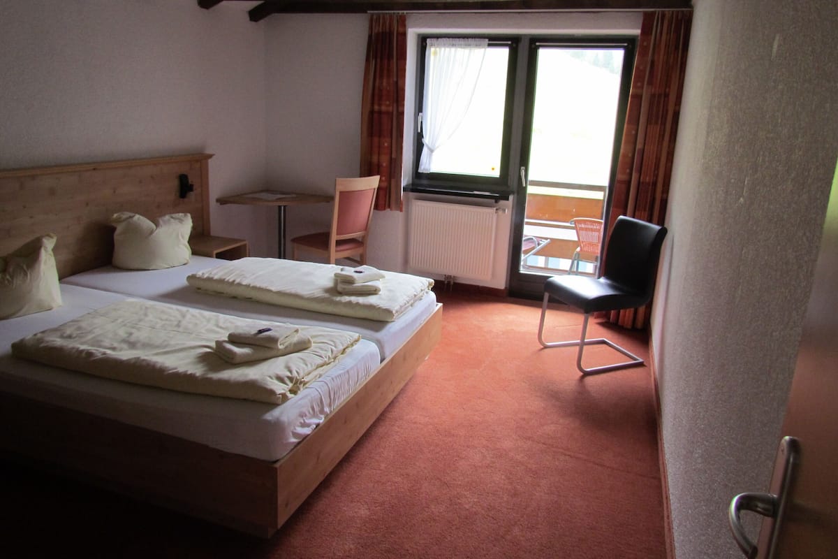 Une chambre d’hôtel avec deux lits, une petite table, une chaise et une vue sur l’extérieur.