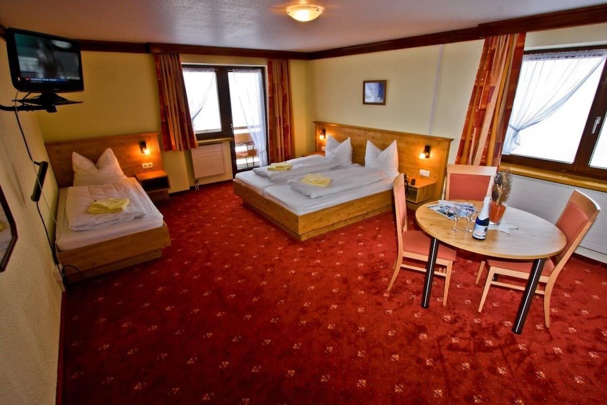 Une chambre d’hôtel avec deux lits, une petite table avec des chaises, une télévision et une fenêtre avec des rideaux.