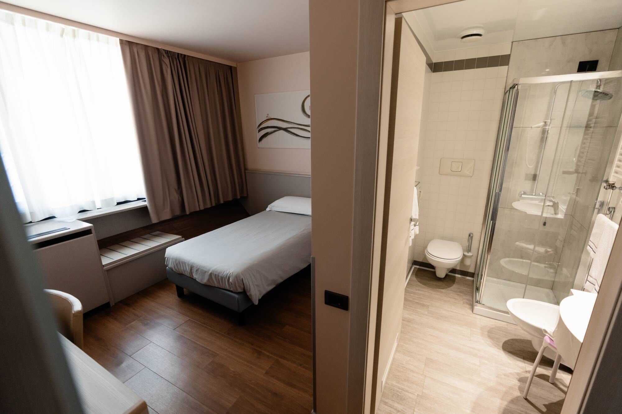 Une chambre d’hôtel comprenant un lit, un bureau, une fenêtre avec des rideaux et une salle de bain avec douche et toilettes.