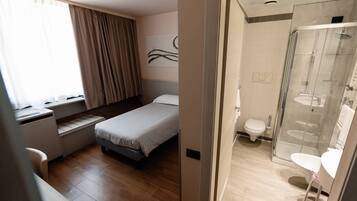 Une chambre d’hôtel comprenant un lit, un bureau, une fenêtre avec des rideaux et une salle de bain avec douche et toilettes.