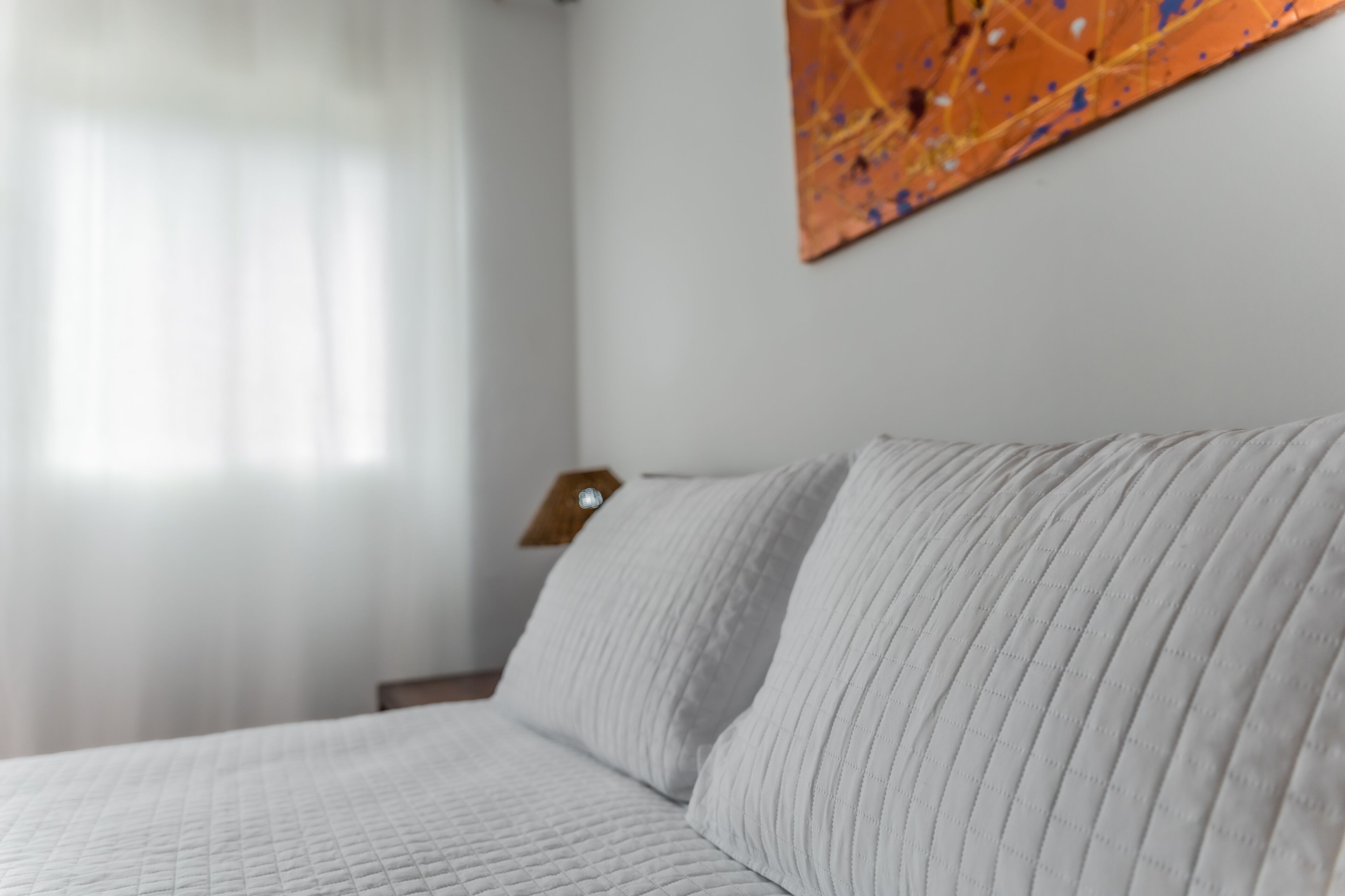 Un lit avec une couverture matelassée et un oreiller, une table de chevet en bois avec une lampe, et un tableau accroché au mur.
