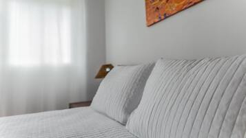 Un lit avec une couverture matelassée et un oreiller, une table de chevet en bois avec une lampe, et un tableau accroché au mur.