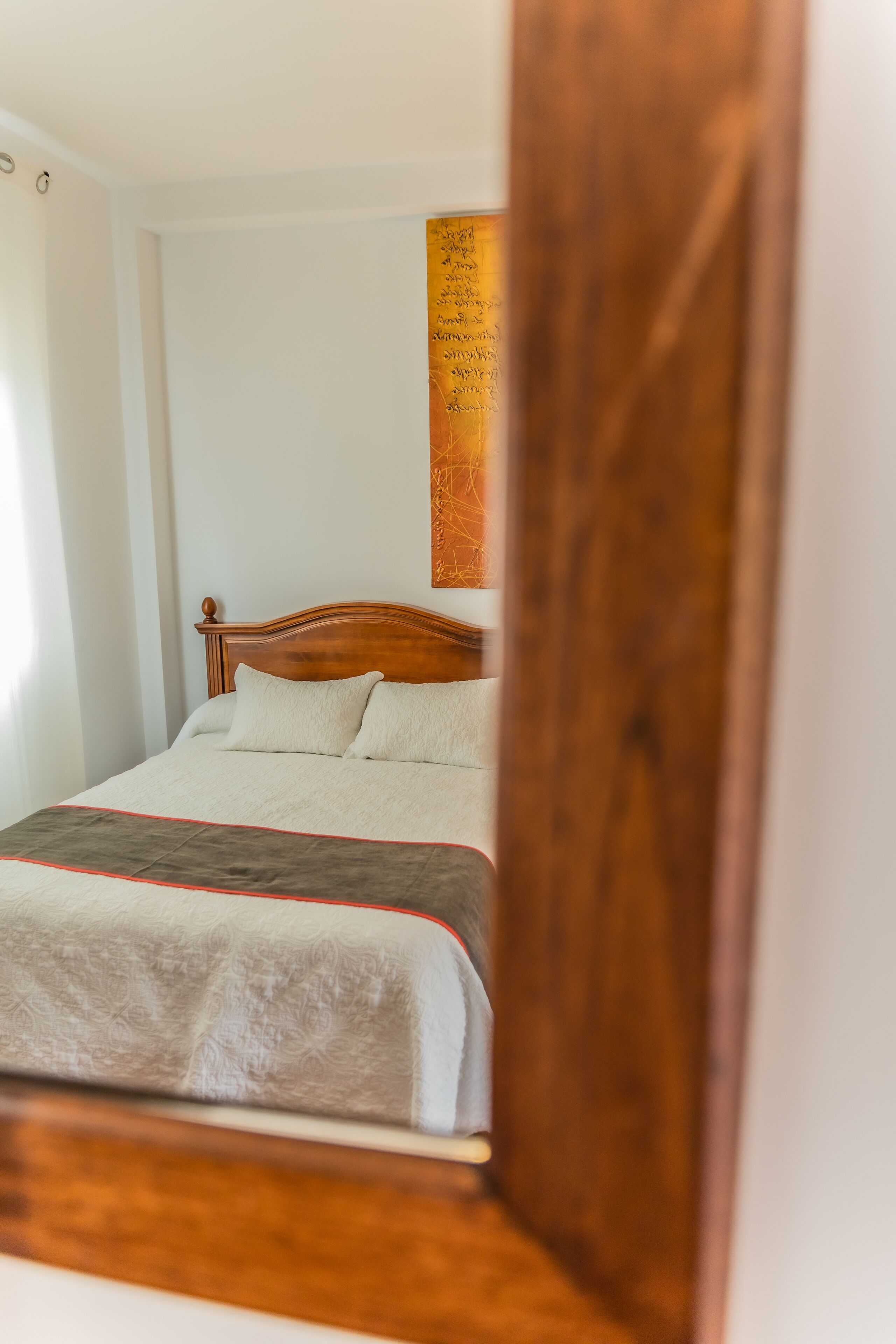 A bed with a wooden headboard, a white and grey bedspread, and a red trim.