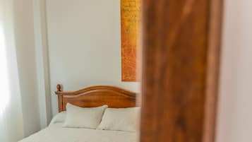 A bed with a wooden headboard, a white and grey bedspread, and a red trim.