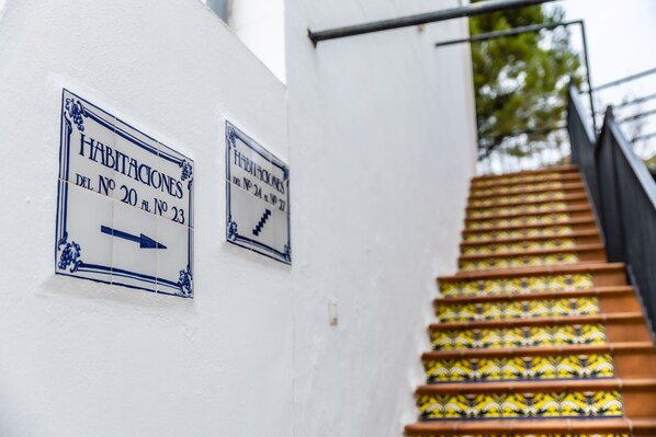 Una escalera con baldosas estampadas que conduce a un edificio. Hay dos carteles en la pared que indican números de habitaciones.