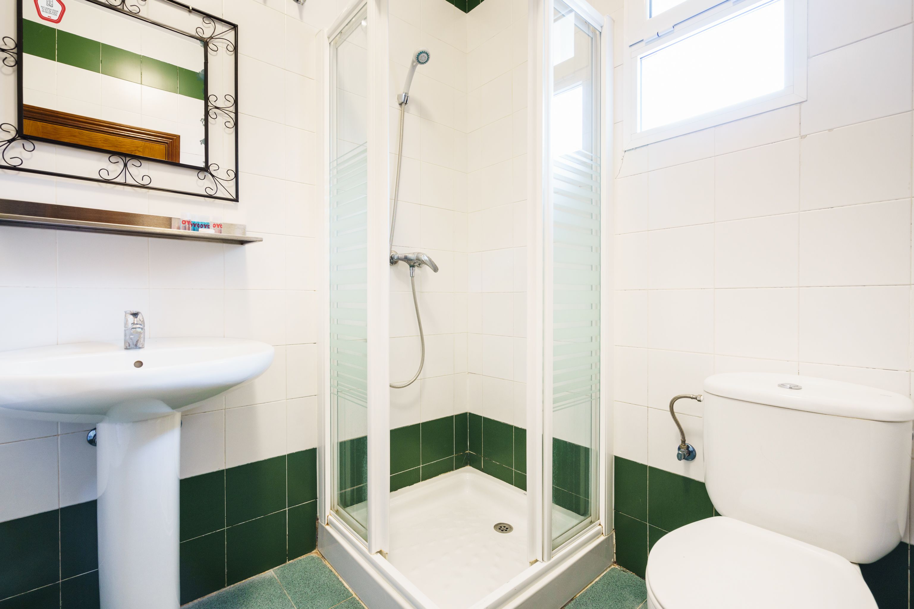 A bathroom with a shower, sink, toilet, and a mirror with a decorative frame.