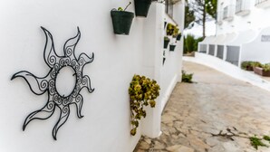 A white building with a decorative metal sun design on the wall, potted plants, and a stone-paved pathway. - Hotel Las Errizas by Vivere Stays (Alcala del Valle)