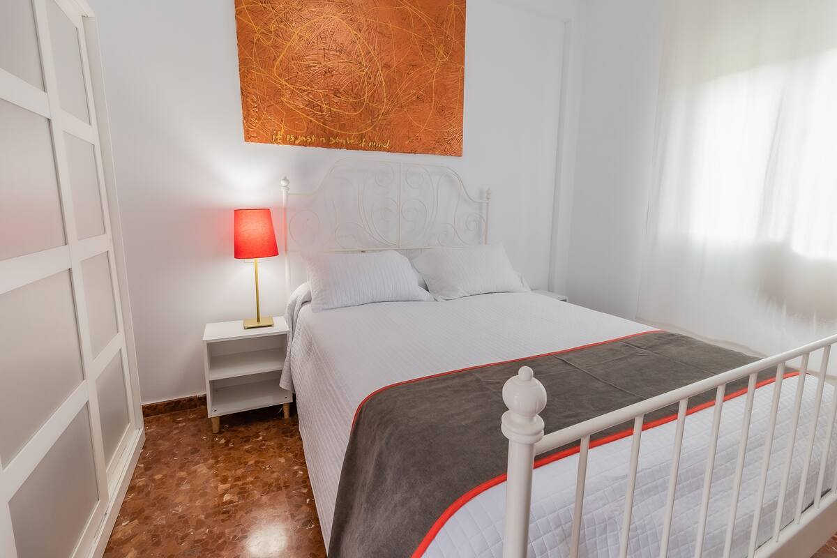 Ein ordentlich eingerichtetes Schlafzimmer mit Bett, Nachttisch, Lampe und einem Wandbild.