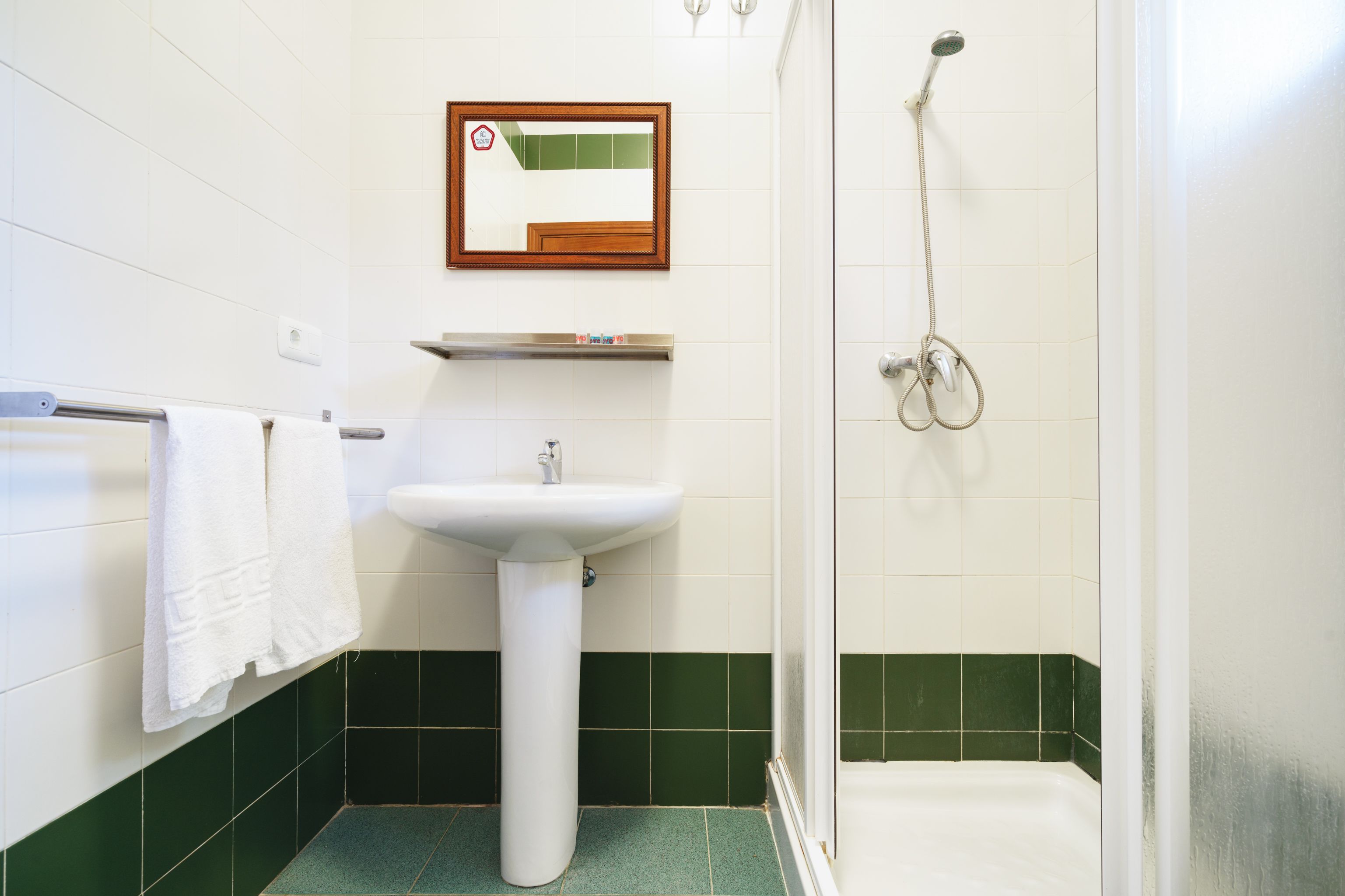 A bathroom with a white sink, a mirror, a shower, and green-tiled walls.