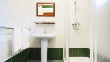 A bathroom with a white sink, a mirror, a shower, and green-tiled walls.