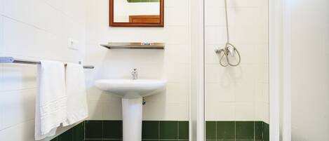 Un baño con lavamanos blanco, espejo, ducha y paredes con azulejos verdes.
